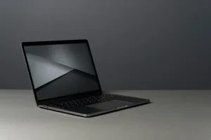 Zbliżenie na trzy eleganckie laptopy z cienkimi ramkami, ustawione na drewnianym biurku w nowoczesnym biurze. Idealne połączenie stylu i dobrej ceny.